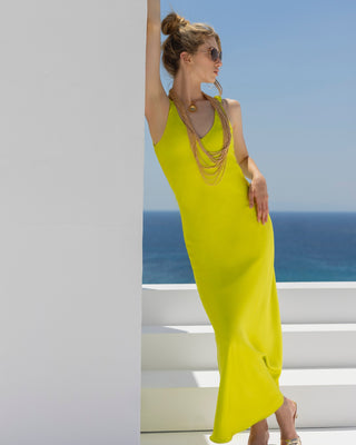 Woman in a bright yellow dress standing by a white wall with ocean view